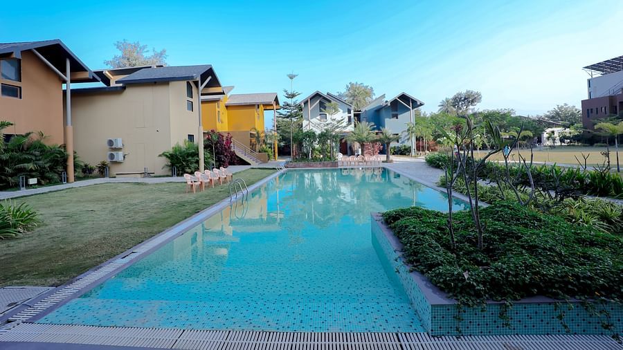 An image of a swimming pool surrounded by houses, plants, and trees - Pride Resort Ambaji